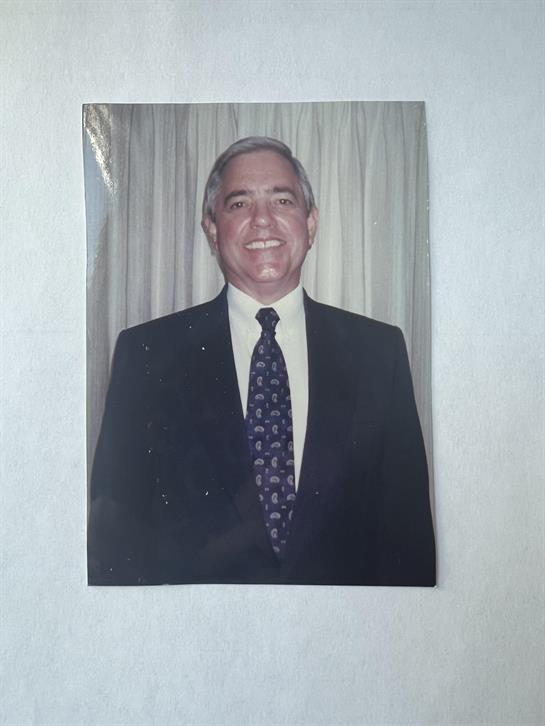 A smiling man dressed in a formal suit poses confidently for the camera indoors.