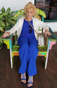 A senior woman sits in a vibrant chair, dressed in blue, enjoying a peaceful moment outdoors.