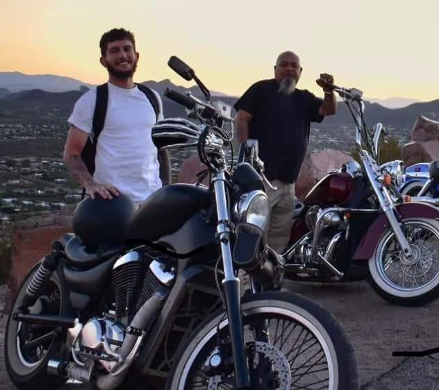 Two friends pose by their motorcycles on a mountainside overlook at sunset, enjoying the view.