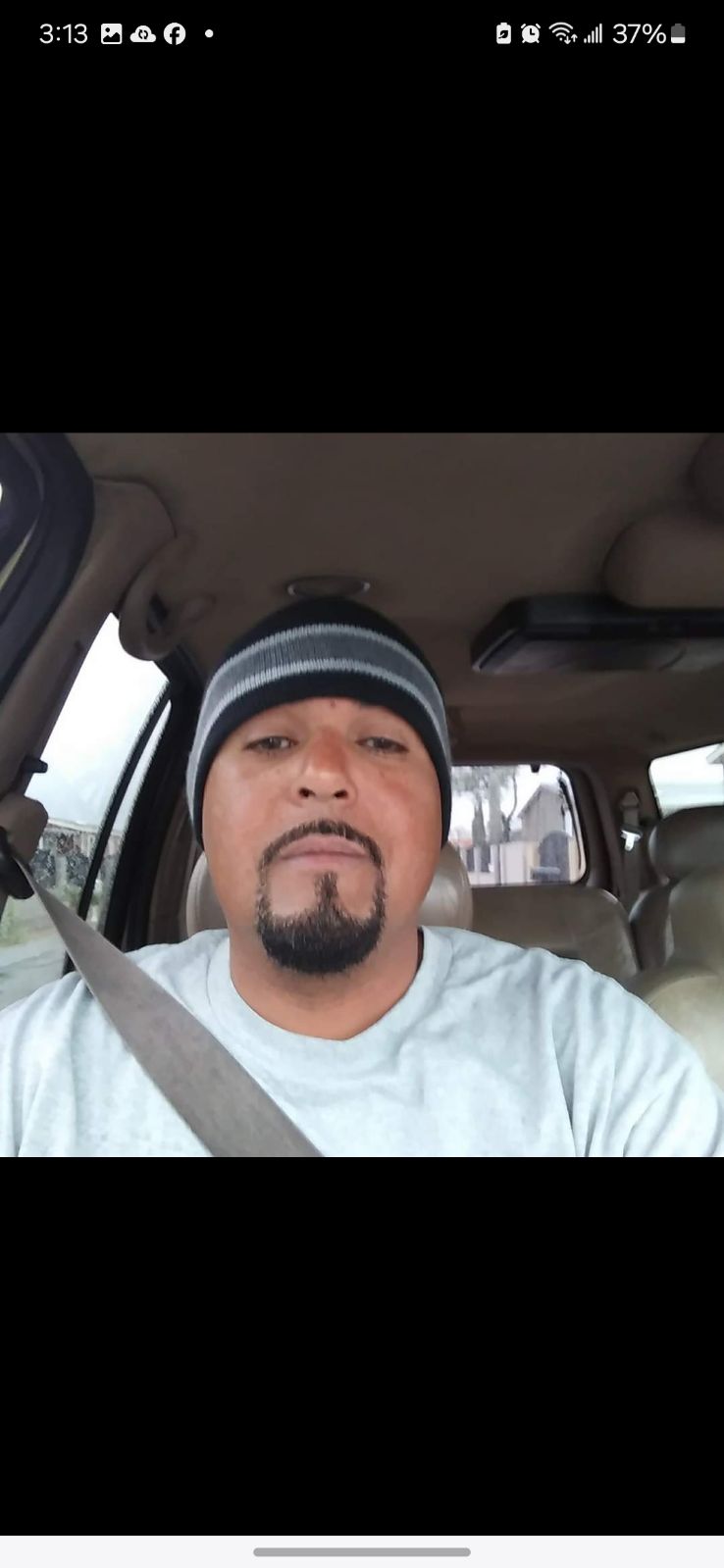 A man is sitting in the driver's seat of a car while wearing a beanie and looking at the camera.