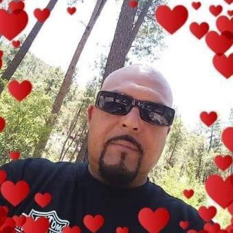 A man stands in a green forest with sunglasses on and heart shapes around him. He looks content.