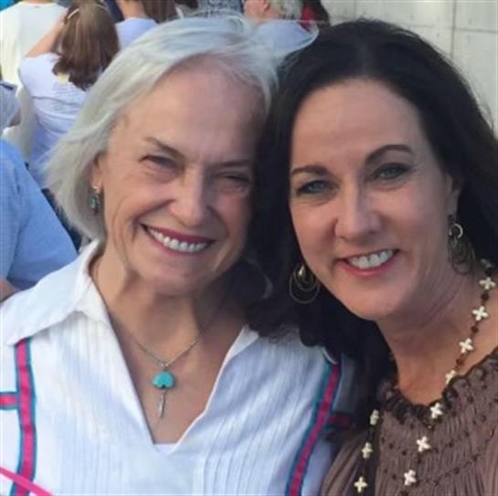 Two friends enjoy a light-hearted moment at a local summer gathering, surrounded by people.