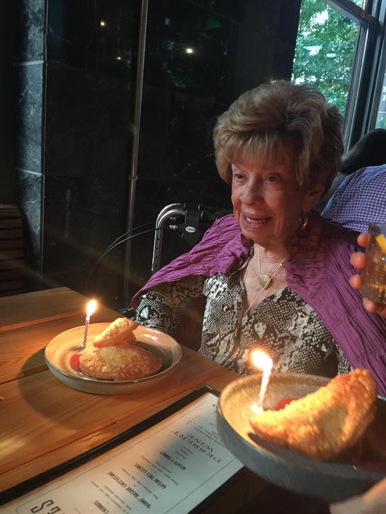 A woman basks in joy as candles flicker atop her cake at a cozy restaurant table.