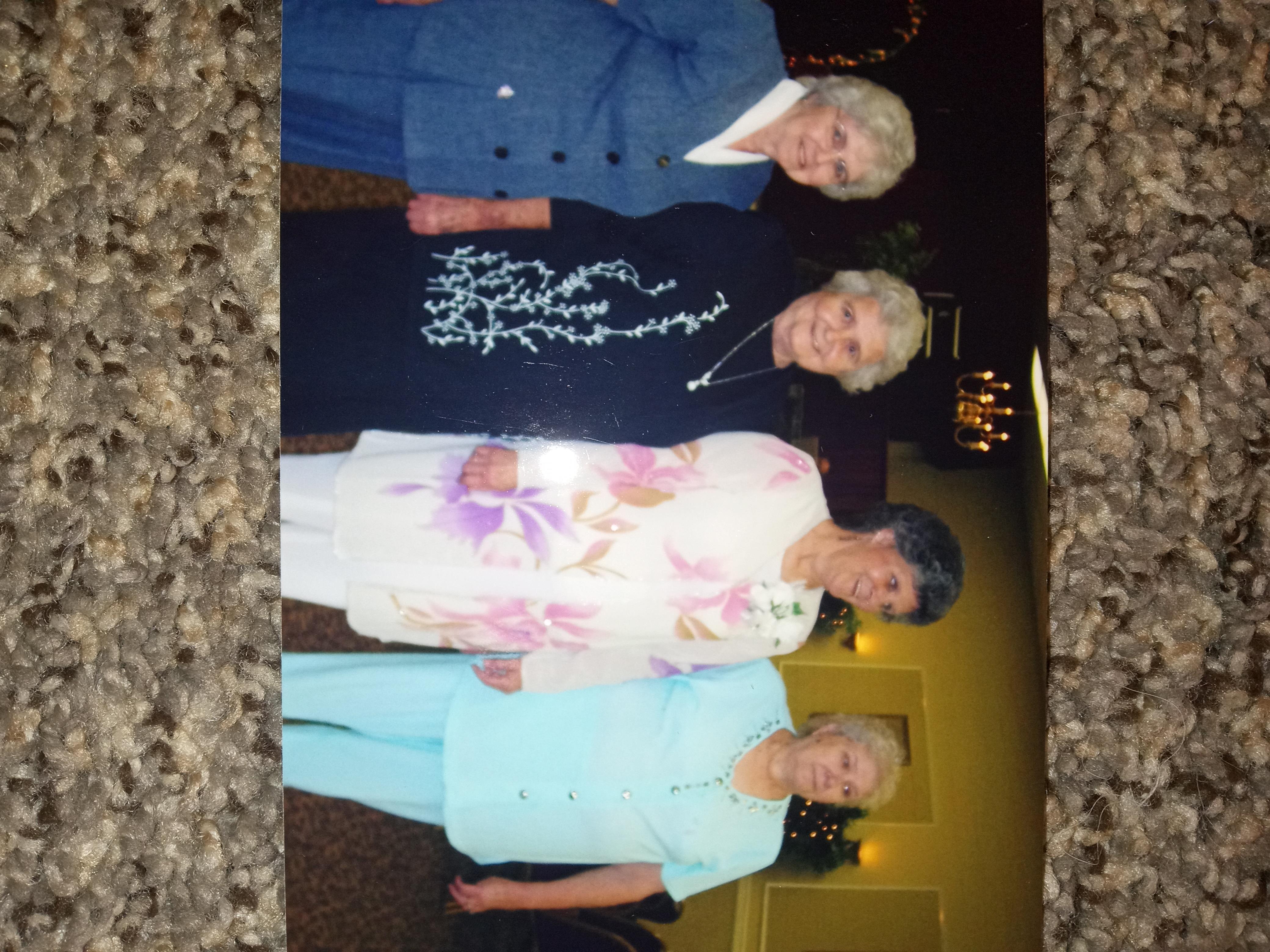 Four women dressed in formal attire smile while posing together at an event.