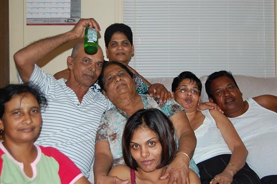A group of friends and family enjoys laughter and drinks in a warm living room atmosphere.