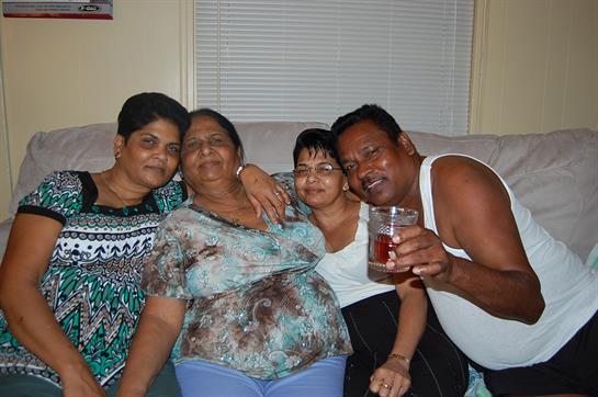 Four family members share smiles and laughter while relaxing on a couch at home.