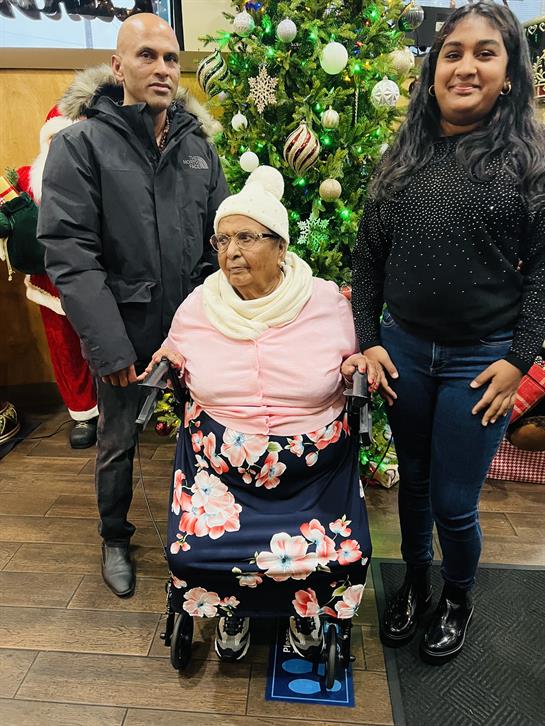 Three family members stand together celebrating near a beautifully decorated Christmas tree.