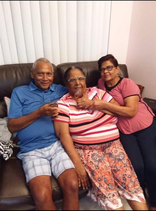 Three family members enjoying quality time together while sitting on a couch, smiling and laughing.