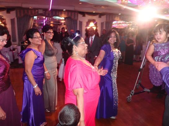 Women in beautiful gowns dance joyfully at a crowded celebration in a festive atmosphere.