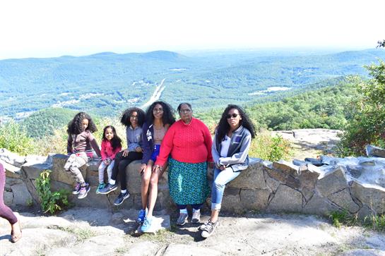 Friends gather on a rocky ledge, admiring the expansive mountain view under clear skies.