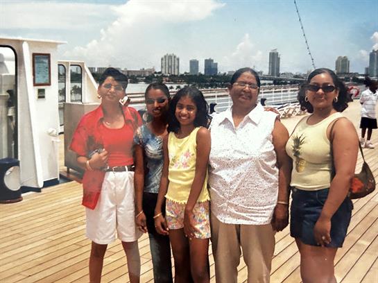 Five women smile on a boat, enjoying a sunny day by the harbor with a skyline in view.