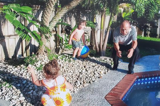 Two kids enjoy playing in a bright backyard while an adult watches and interacts with them.
