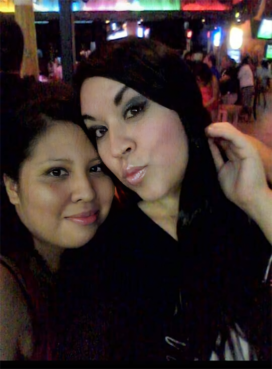 Friends smile while spending time at a lively bar filled with colorful lights and joy.