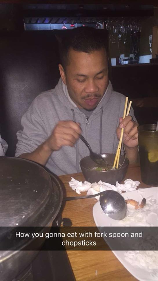 A man struggles to eat from a bowl using multiple utensils at a dining table.