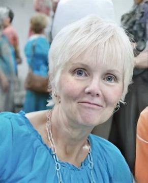 A cheerful woman with short blonde hair enjoys a community gathering, happily interacting.