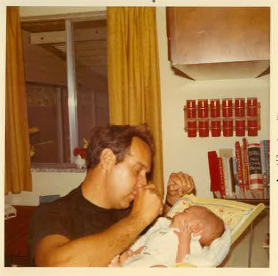 A loving father gently interacts with his newborn in a cozy, book-filled home.