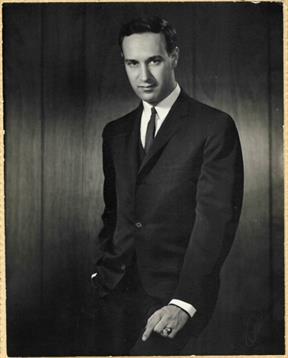 A well-dressed man stands stylishly with one hand in his pocket, exuding charisma.