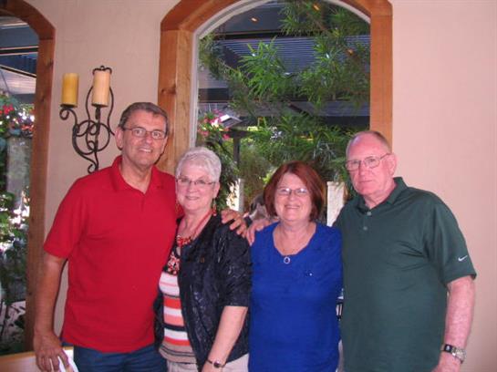 Four friends stand together in a welcoming indoor space, smiling and chatting happily.