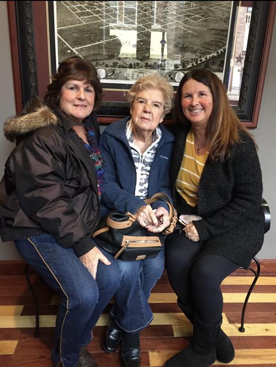 Three women gather and share smiles in a comfortable indoor space, creating a joyful moment.
