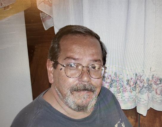 An elderly man with glasses smiles warmly in a cozy indoor setting.