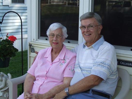 Two smiling individuals sit closely on a porch, sharing moments of joy and companionship.