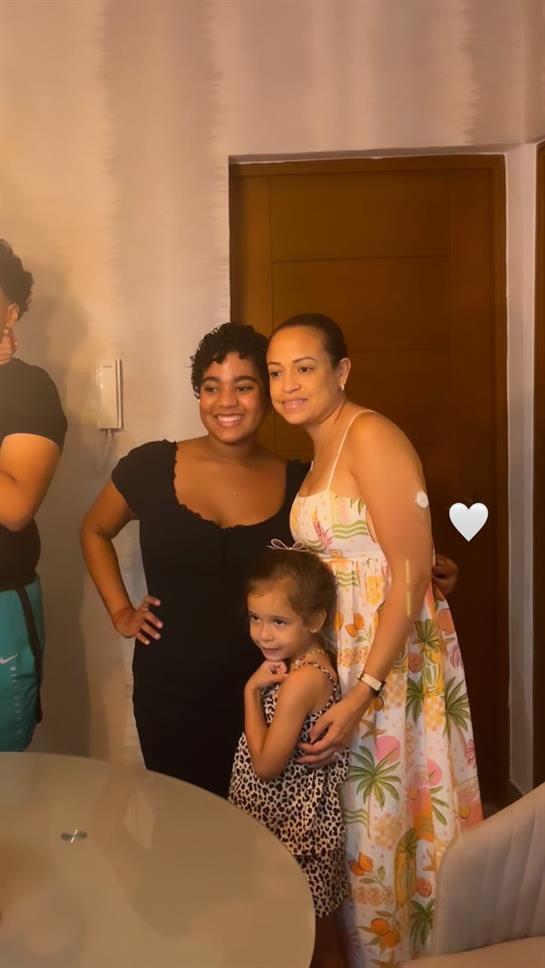 Three women and a young girl stand together, smiling joyfully in a warm room.