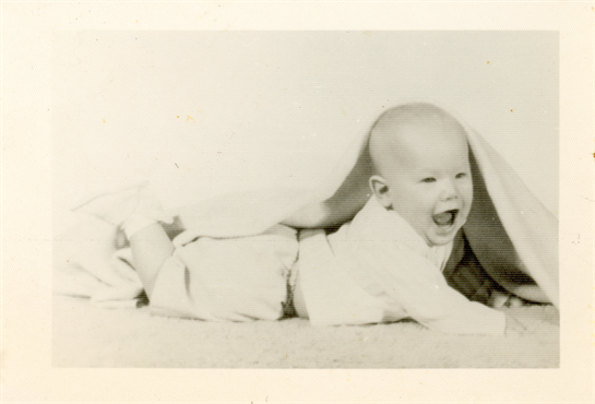 A cheerful baby crawls beneath a soft blanket, expressing happiness in a cozy environment.