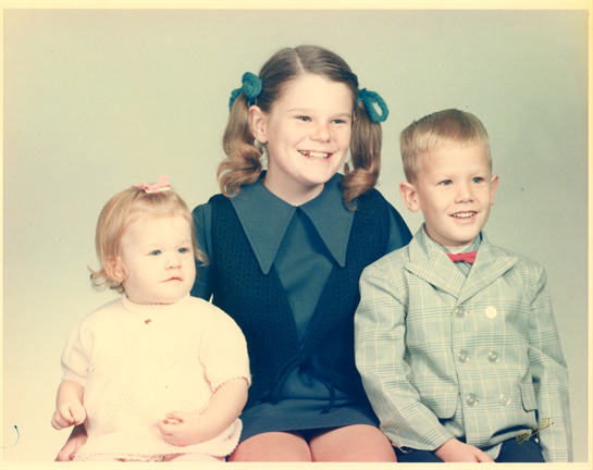 Three children smile at the camera, dressed in colorful outfits, capturing a playful moment of joy.