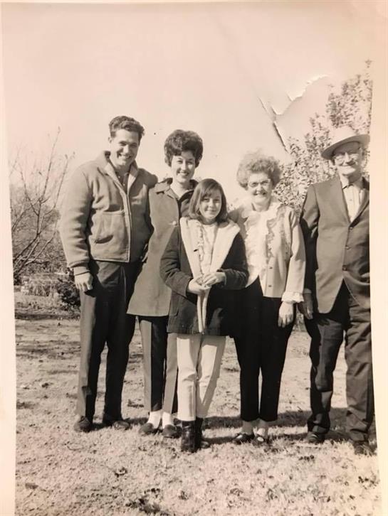 Five individuals stand together outdoors, smiling in a warm, sunny atmosphere.