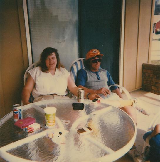 Two friends enjoy refreshments while seated at a round table outside a building.