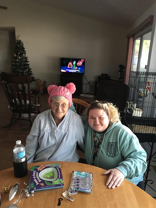 Elderly woman and young woman sit together at a table, smiling and sharing a moment of joy.