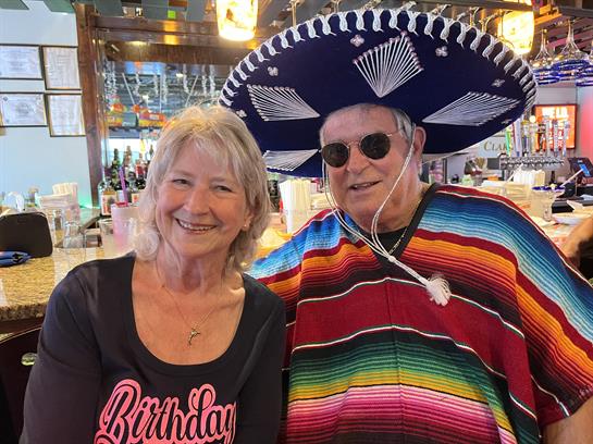 Two cheerful individuals pose together in colorful attire during a lively birthday celebration.