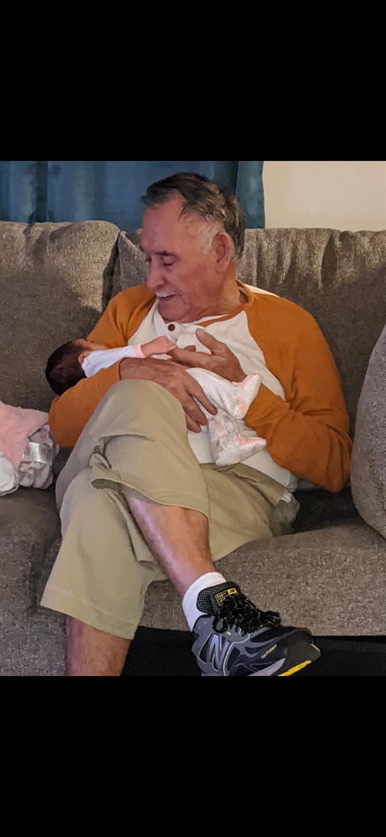A grandfather cradles his newborn granddaughter on a soft sofa, radiating warmth and love.