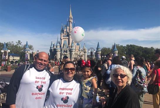 Four family members celebrate with matching shirts in front of a castle on a clear day.