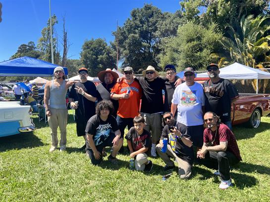 Friends gather joyfully at an outdoor car event, surrounded by classic cars and tents.