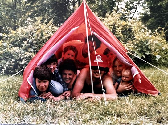 A lively group of friends enjoys their time inside a bright red tent on a sunny day.