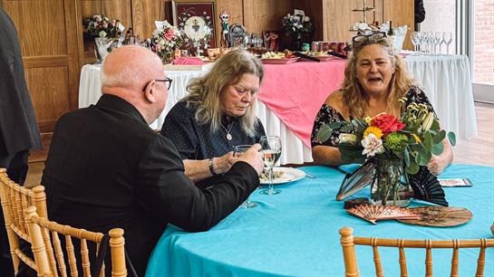 Three adults engage in lively conversation while enjoying refreshments at a festive gathering.