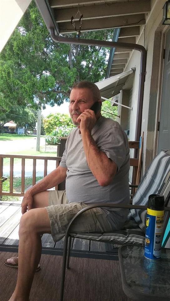 A man is conversing on the phone while seated comfortably on his porch.