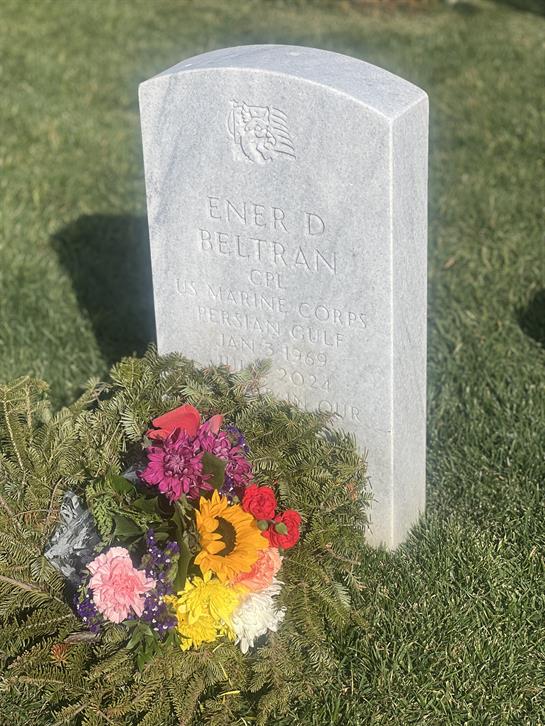 A marble gravestone marks the resting place of Ener D Beltran, adorned with colorful flowers.