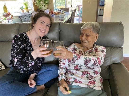 Two women toast with drinks while sitting comfortably on a couch, enjoying each other's company.