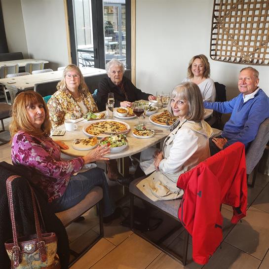 A group of friends interacts over a shared meal at a cozy restaurant setting.