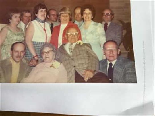 A joyful family gathering takes place indoors with multiple generations posing closely together.