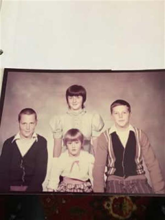 Four children stand together in a formal portrait, dressed in nostalgic attire from the early 1970s.