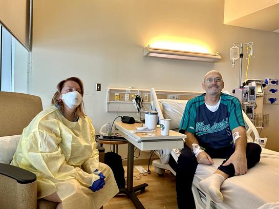 A patient sits on the bed while a caregiver engages with them in the hospital room.