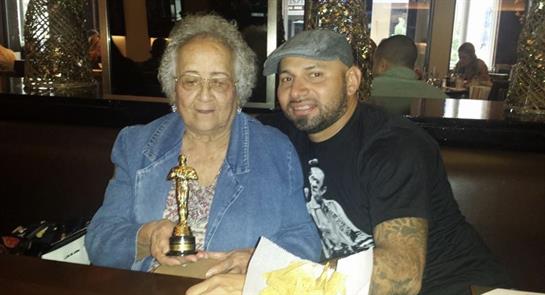 Grandmother proudly holds a trophy while posing with her grandson in a warm restaurant setting.