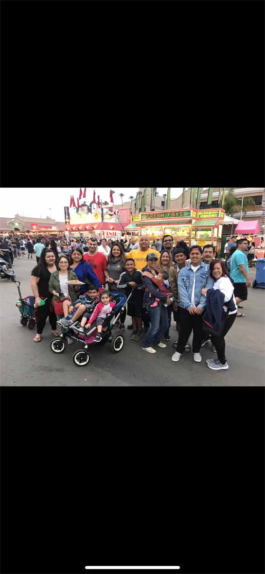 A large group gathers for a fun time at a festival with food stalls and rides in the background.