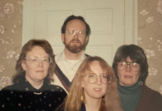 Four people stand together, smiling while dressed in casual attire, showcasing a cheerful moment.