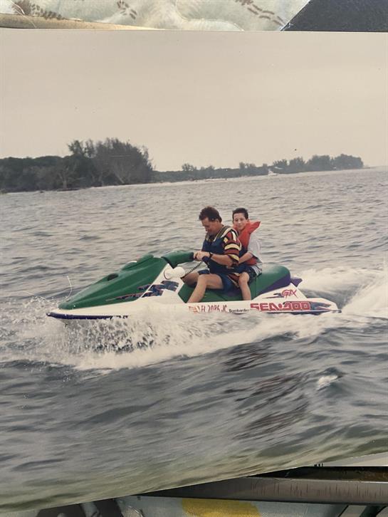 Two boys are excitedly riding a jet ski on the water during a summer day at the lake.