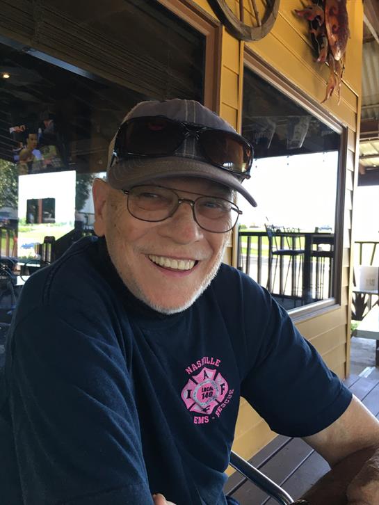 Friendly older man is seated outdoors at a cafe, enjoying the sunny atmosphere with a smile.