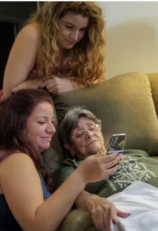 Two younger women gather around an older woman, looking at a smartphone and smiling together.